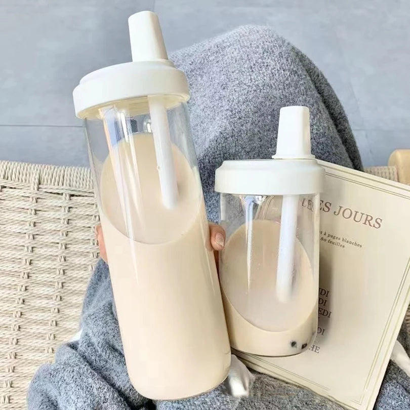 Two beige kawaii water bottles with white straws on a textured surface.