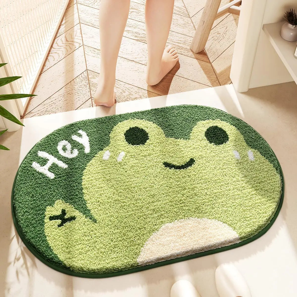 Kawaii green frog-shaped rug with 'Hey' text on a wooden floor.