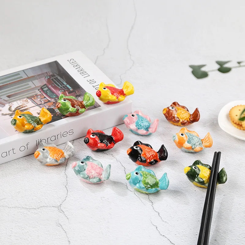 Colorful fish-shaped ceramic kawaii chopsticks holders on a marble surface with a book in the background.