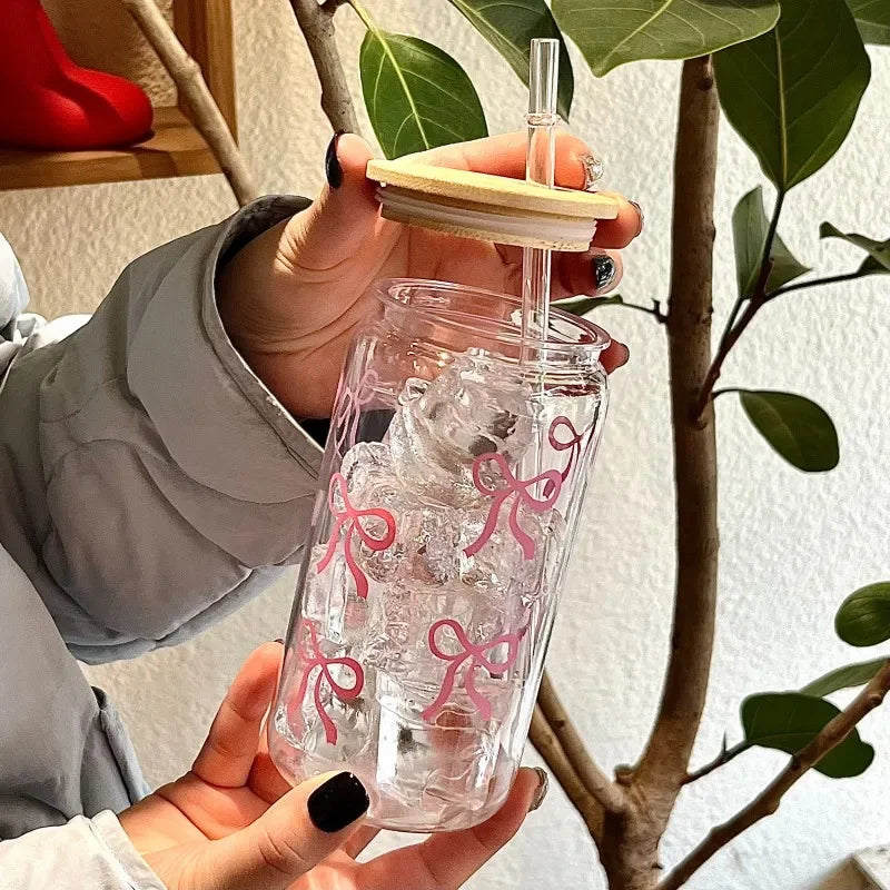 Clear kawaii tumbler with pink designs held by a person, with a plant in the background.