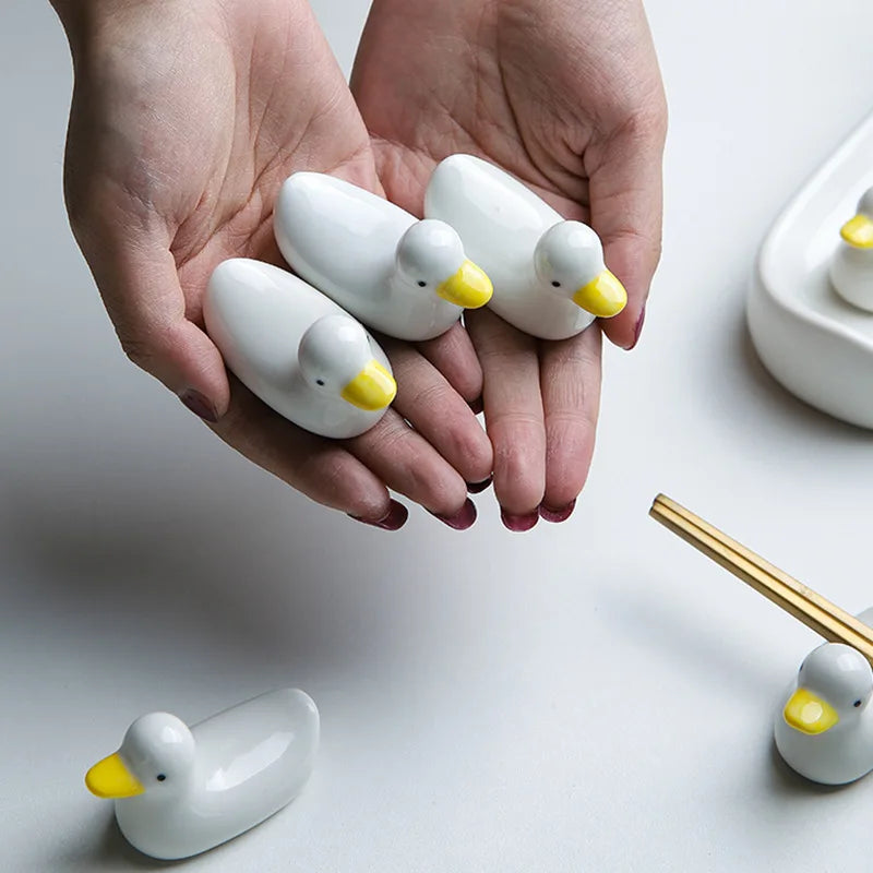 White ceramic ducks kawaii chopstick holders with yellow beaks held in hands on a light background
