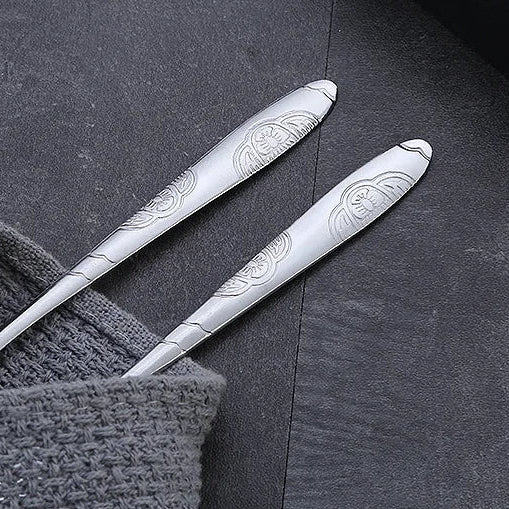 Two silver spoons from a kawaii utensils set with engraved designs on a textured surface.