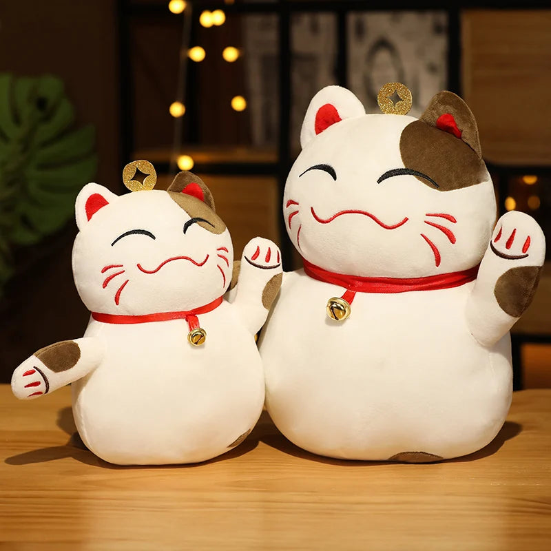 Two kawaii plush Maneki Neko cats on a wooden surface with a blurred background
