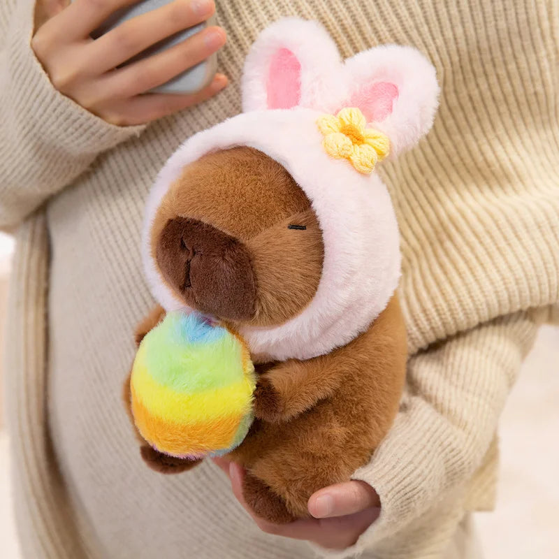 Kawaii plush toy resembling a brown animal in a white outfit with pink ears, held by a person wearing a beige sweater.