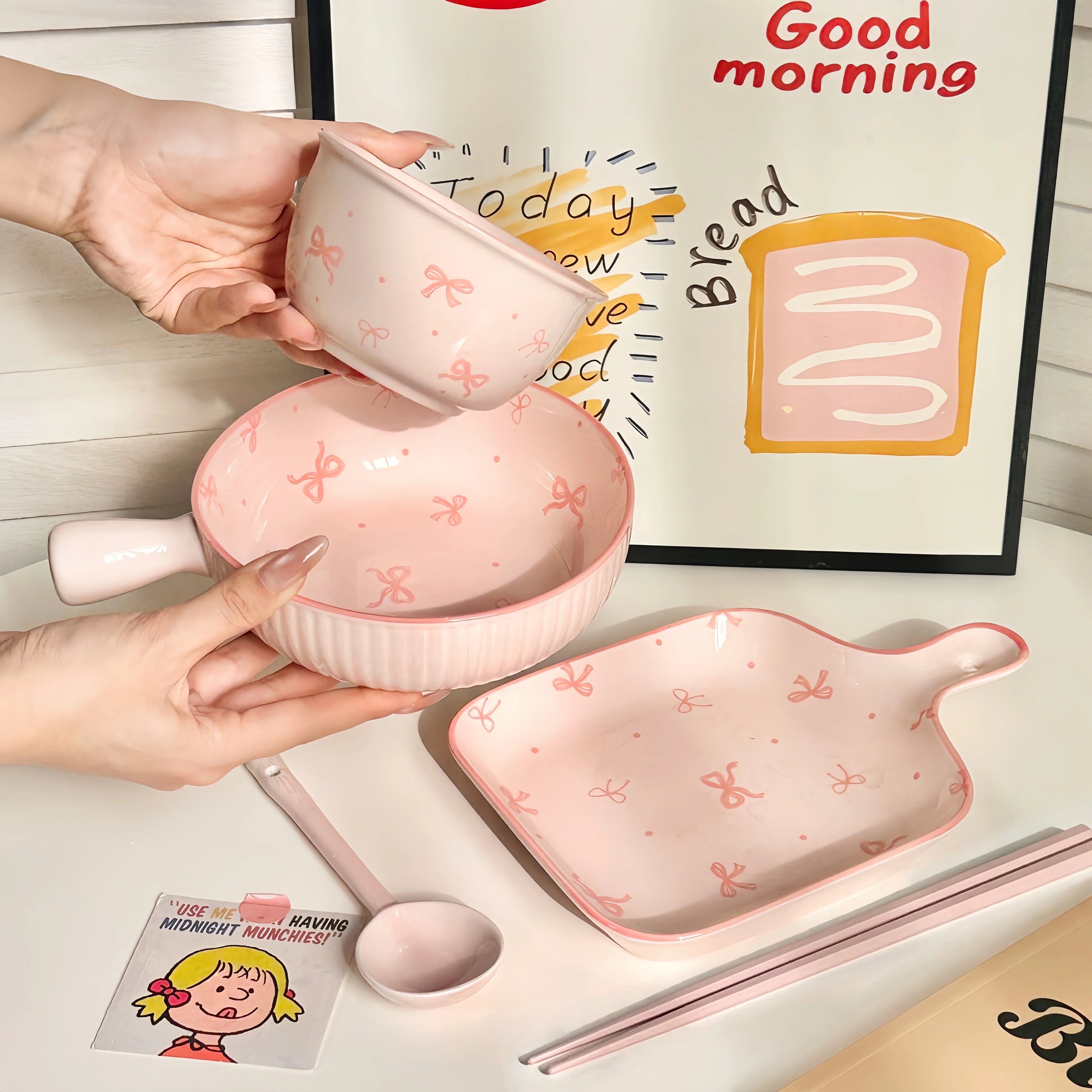 Set of pink ceramic kawaii ramen bowl with bow pattern on a table with a 'Good morning' poster in the background.