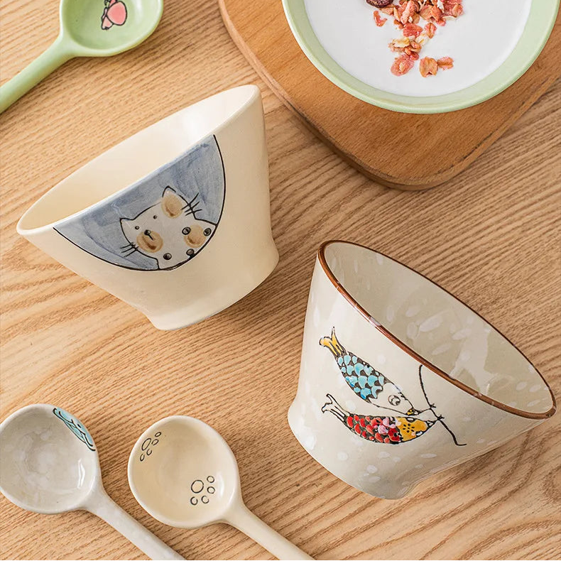Ceramic kawaii ramen bowls and spoons with cat illustrations on a wooden surface