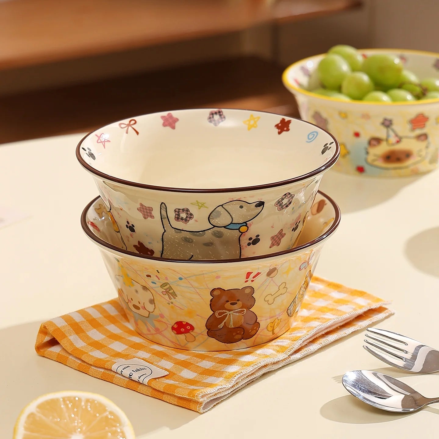 Set of three ceramic kawaii ramen bowls with animal designs on a table with a napkin and fruit.