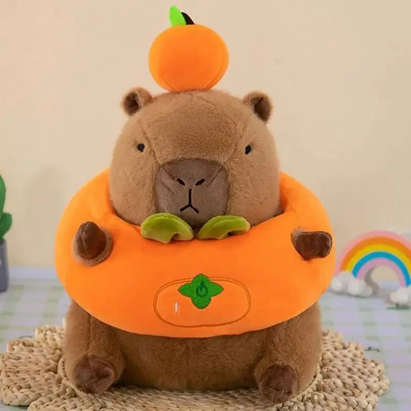 Kawaii plush toy bear in a pumpkin costume with a small pumpkin on its head, sitting on a textured surface with a rainbow and cloud in the background.