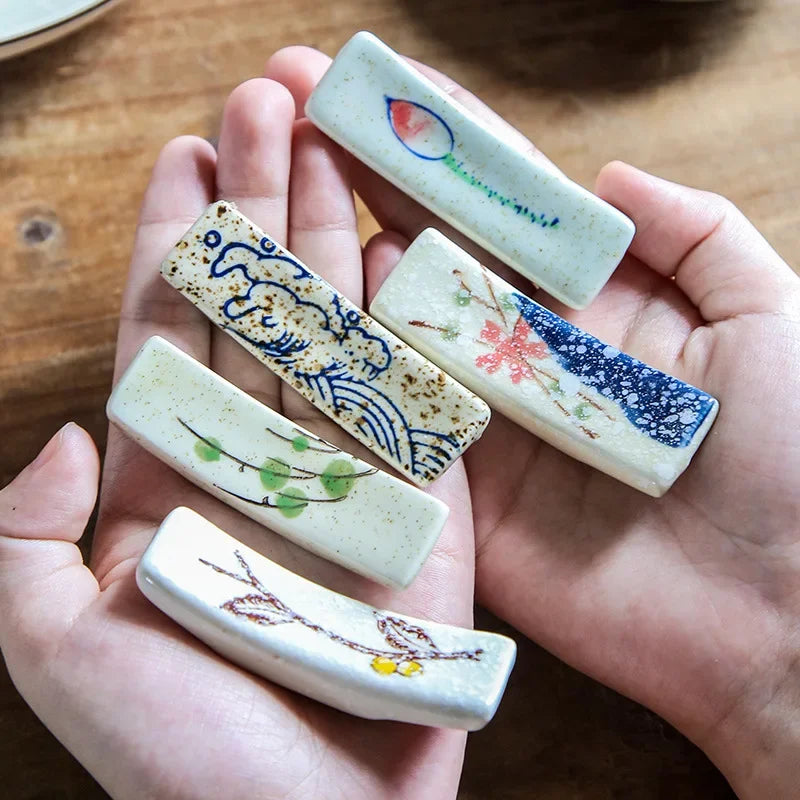 Hand holding five small kawaii chopstick holders with floral designs on a wooden surface