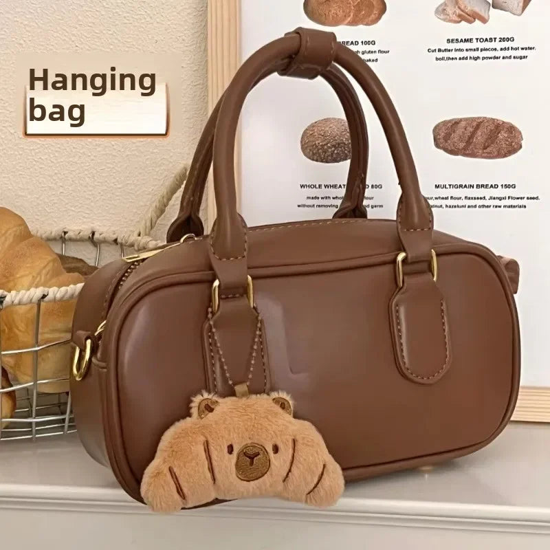 Brown handbag with a kawaii bear-shaped keychain on a surface with bread in the background