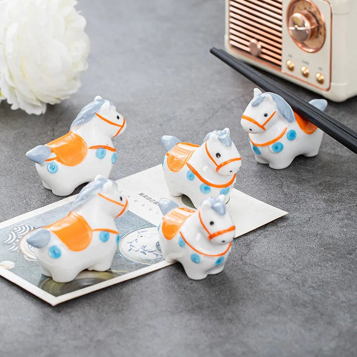 Set of small ceramic horse kawaii chopstick holders on a gray surface with a vintage radio in the background.