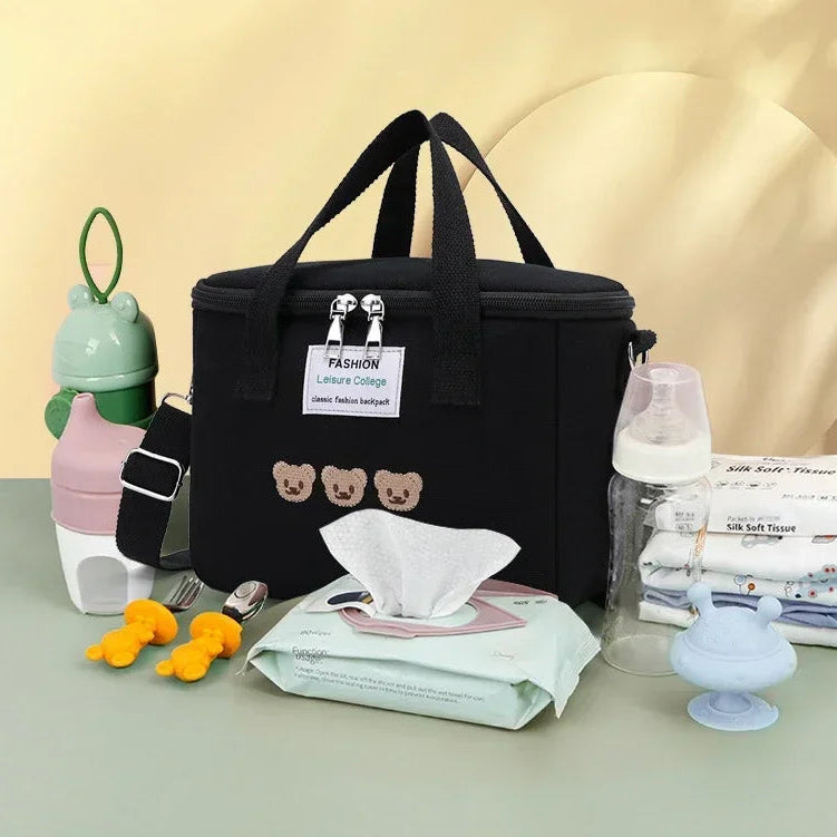 Black kawaii lunch bag with baby care items on a light gray surface against a beige background