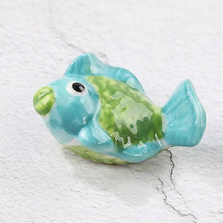 Small ceramic fish kawaii chopstick holders with blue and green colors on a white marble surface