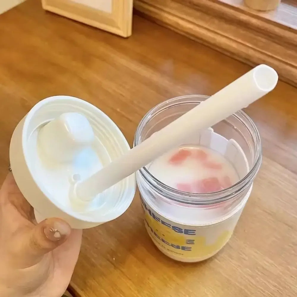 Clear kawaii cup with pink contents and white straw held by a hand on a wooden surface