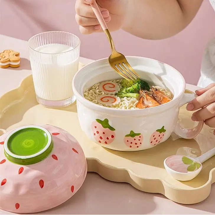 Person eating noodles from a strawberry-themed kawaii bowl with a glass of milk on a pink background