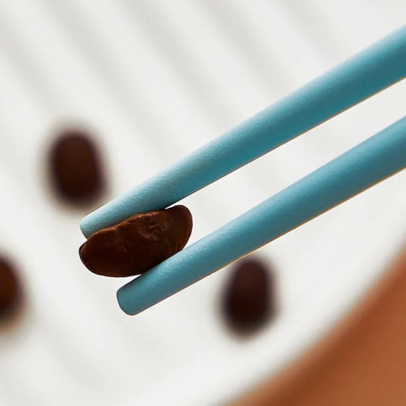 Two kawaii chopsticks holding a coffee bean with blurred coffee beans in the background