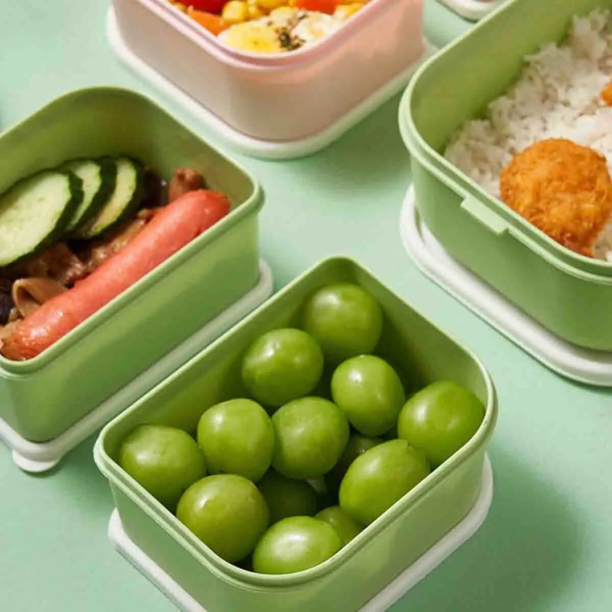 Green kawaii bento boxes with food on a light green surface