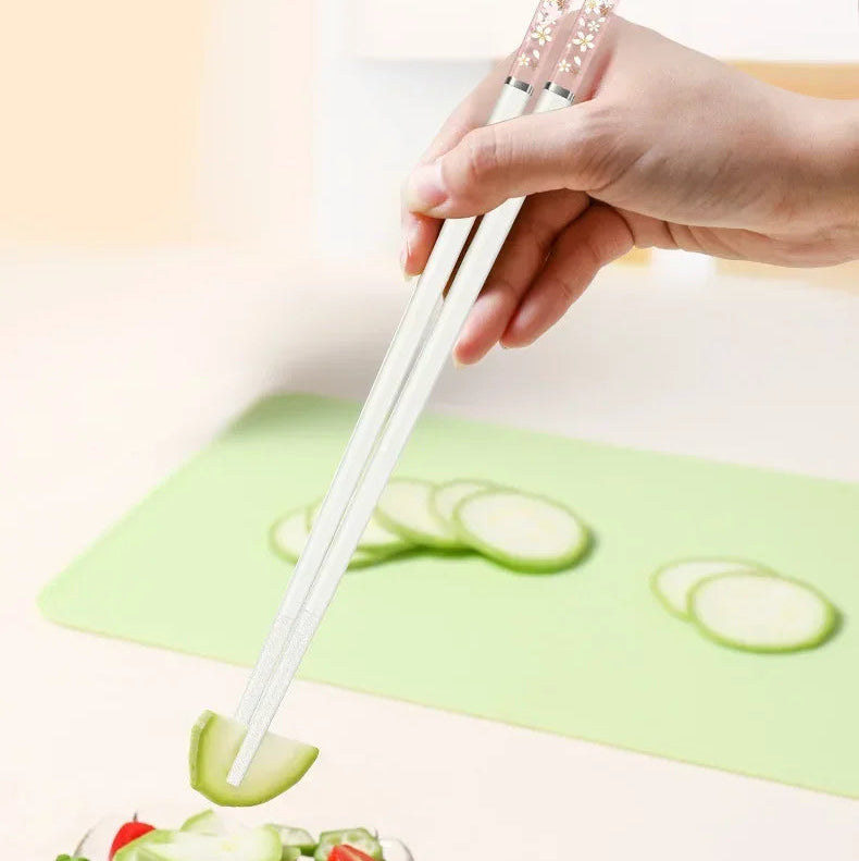 Person using kawaii chopsticks to pick up a slice of cucumber from a salad on a green cutting board.
