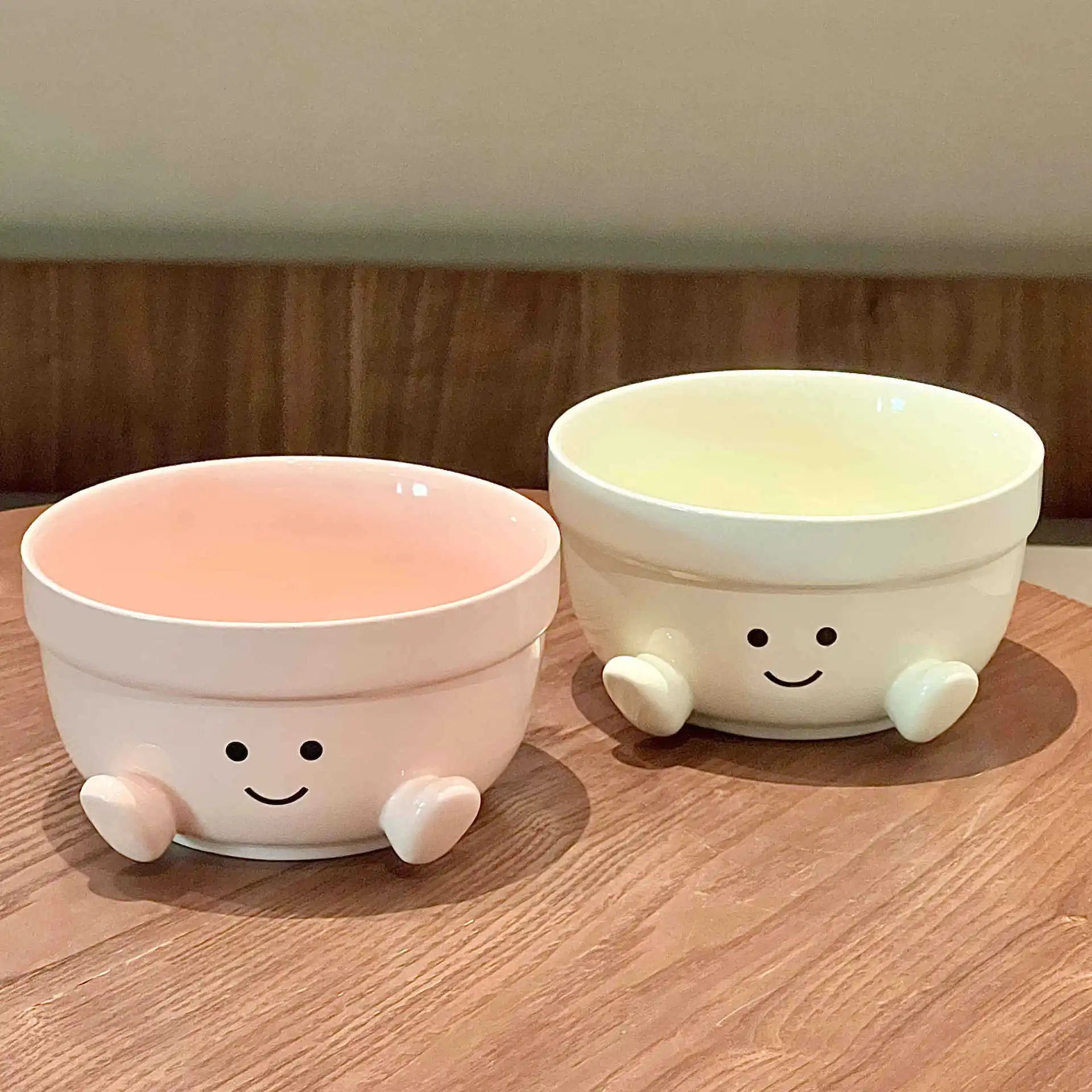 Two ceramic kawaii bowls with smiley face designs on a wooden surface