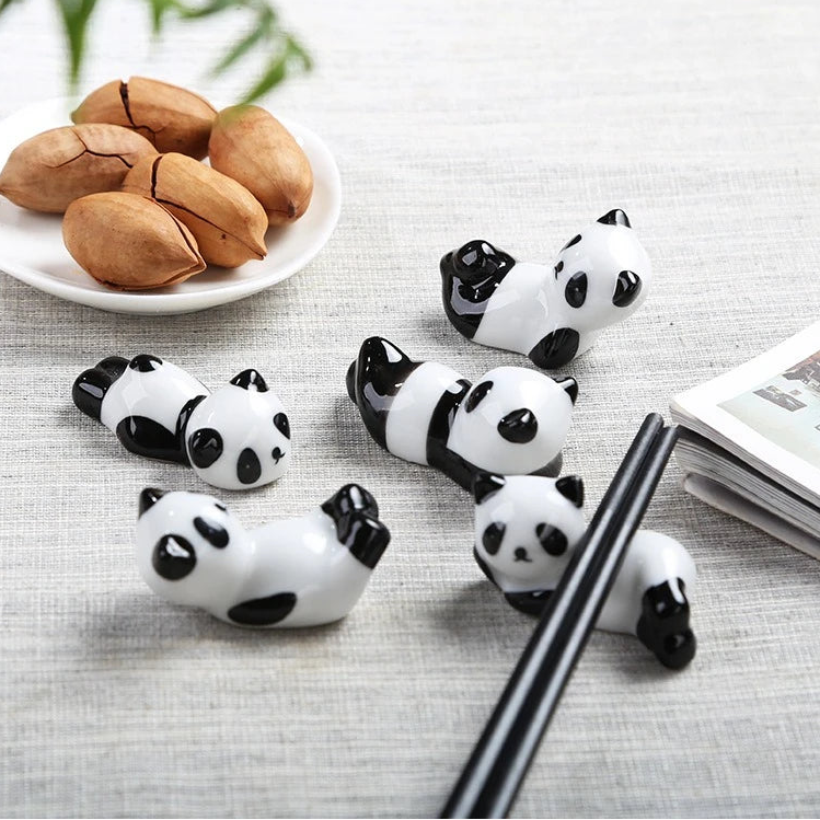 Panda-shaped kawaii chopstick holders on a table with a plate of nuts and a book.