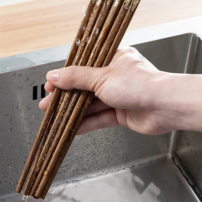 Hand holding a bundle of wooden kawaii chopsticks over a sink