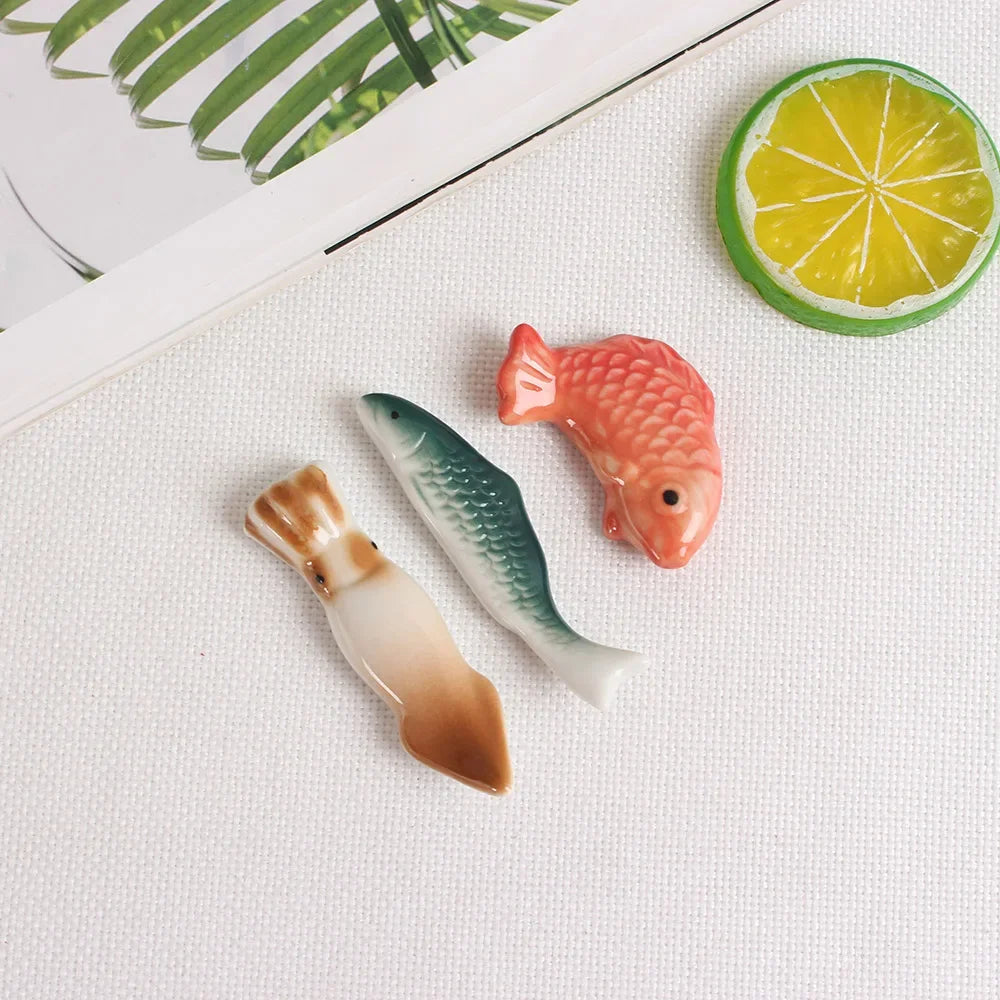 Three fish-shaped kawaii chopstick holders on a textured surface with a lemon slice and green leaves in the background.