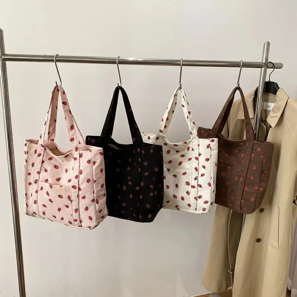 A rack of four tote bags in various colours, all with strawberry pints on them