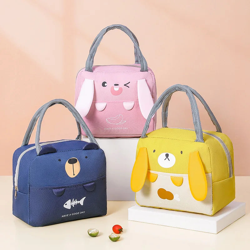 Three cartoon-themed kawaii lunch bags in pink, blue, and yellow on a beige background.