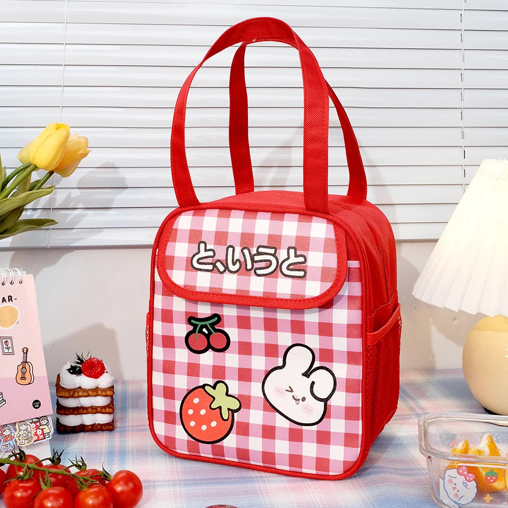 Red and white checkered kawaii lunch bag with cartoon designs on a table with a lamp and flowers in the background.