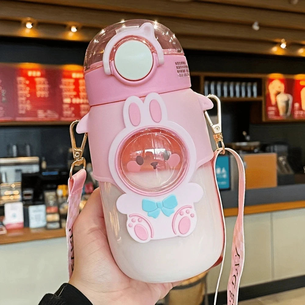 Pink cartoon-style kawaii water bottle with a lanyard held in a hand, blurred coffee shop background