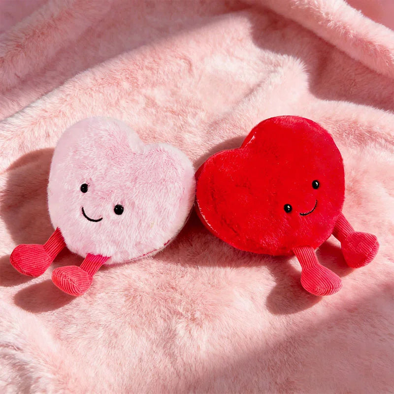 Two heart-shaped kawaii plush toys, one pink and one red, on a pink fluffy background.