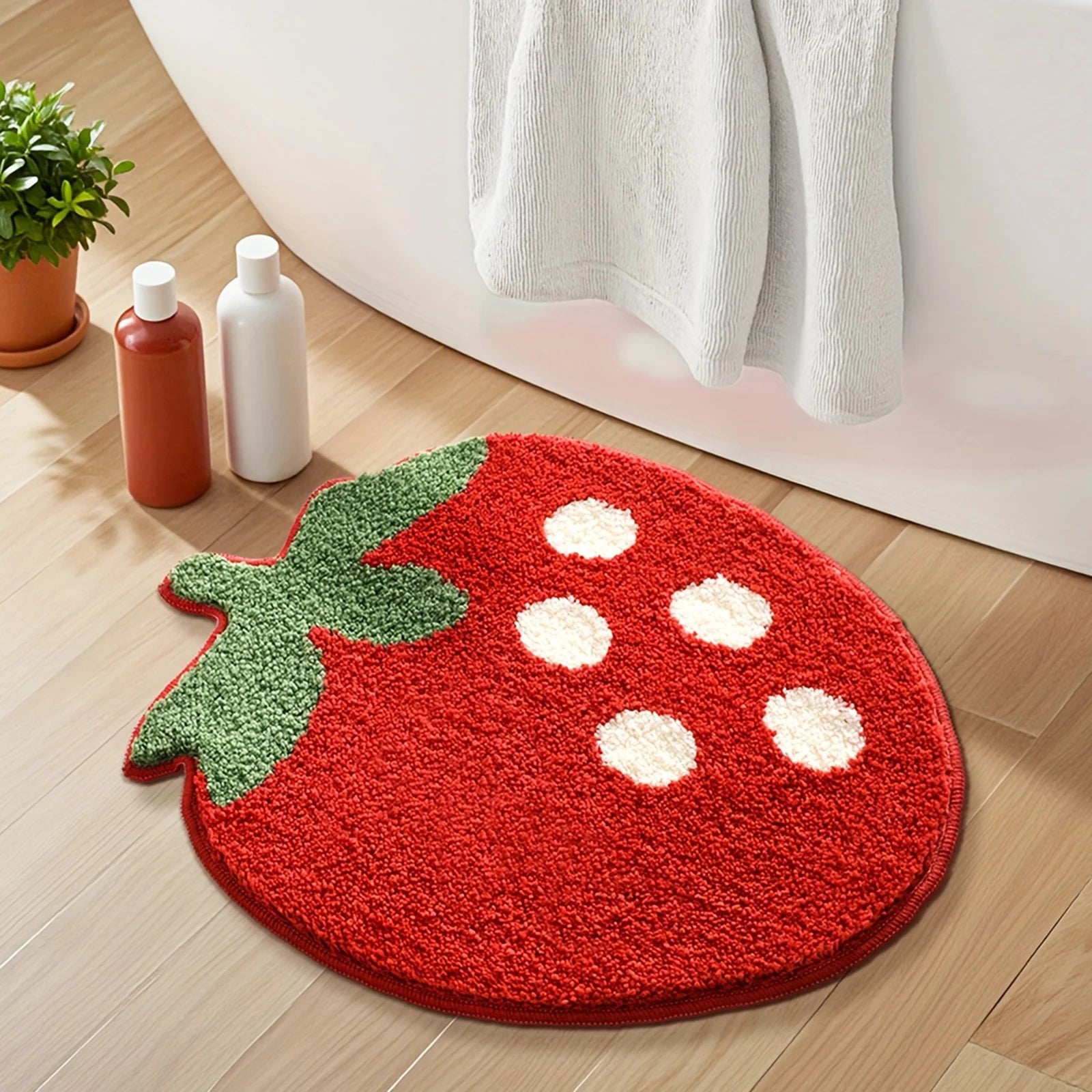 Red strawberry-shaped kawaii rug on a wooden floor with a plant and bottles in the background.