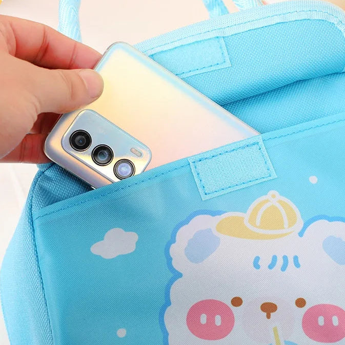Blue kawaii lunch bag with cartoon design and front pocket holding a phone, on a yellow background