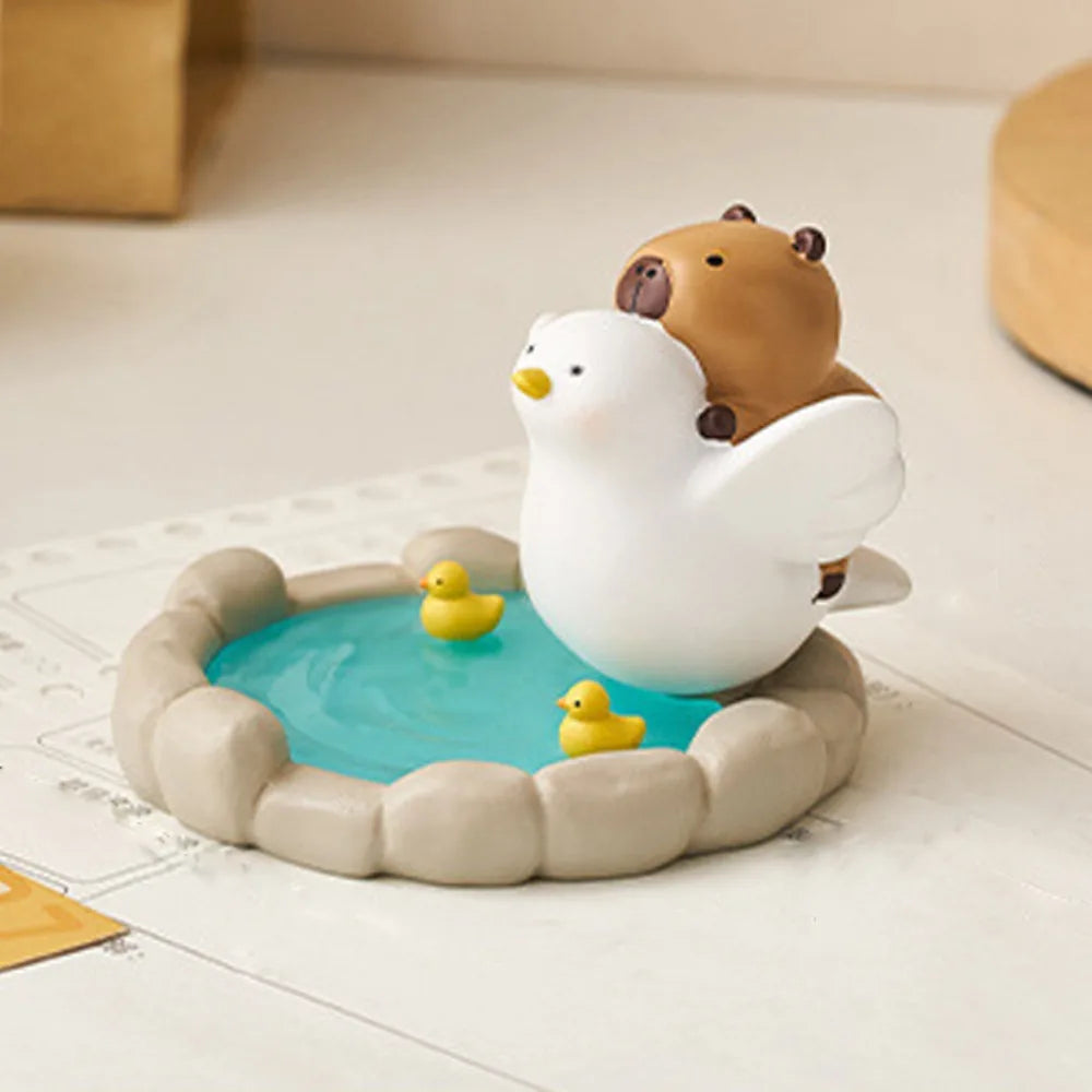 Kawaii capybara phone holder of a bird with a bear on its back, sitting in a small pool with two rubber ducks.