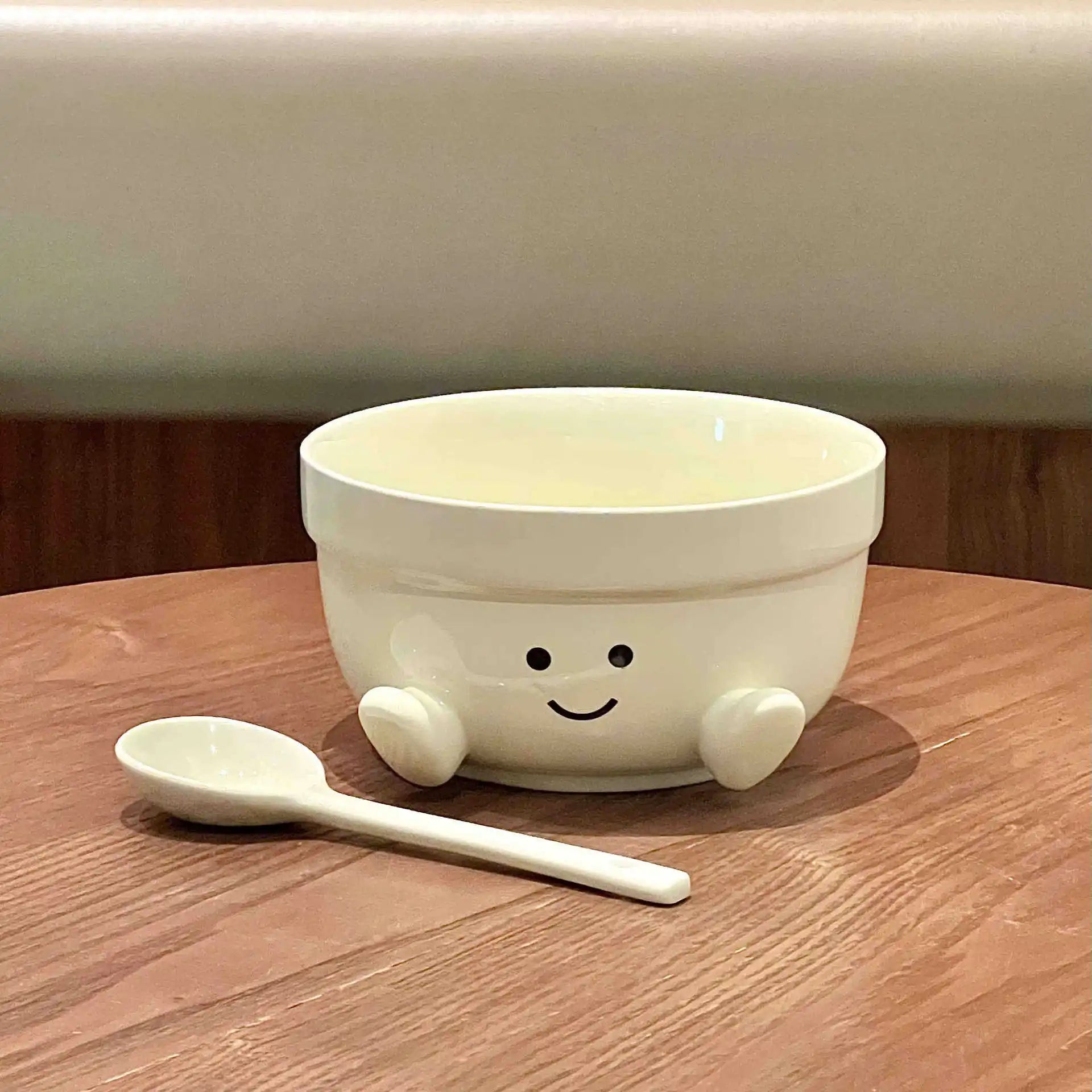 White ceramic kawaii bowl with a smiley face and legs, accompanied by a white spoon on a wooden surface.