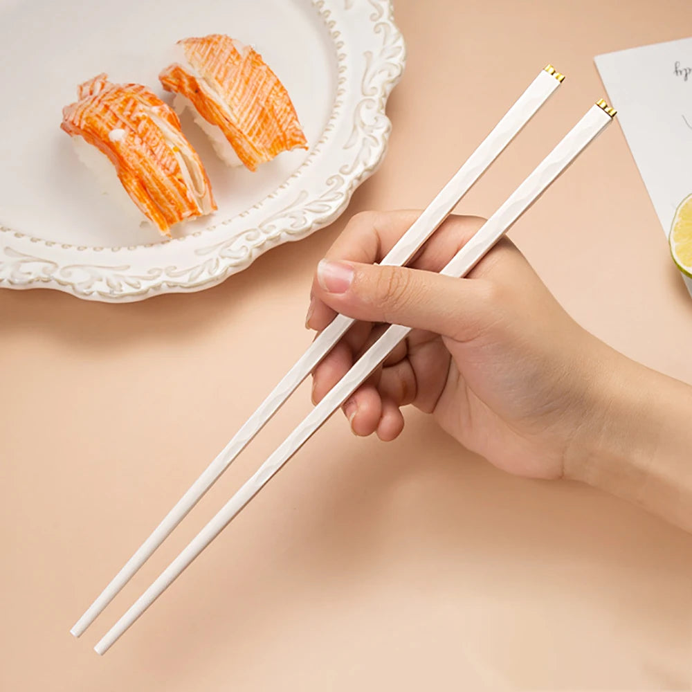 Hand holding white kawaii chopsticks with sushi in the background