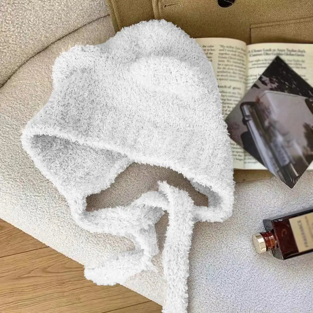 White fleece Kawaii hat draped over a surface with a book and bottle in the background