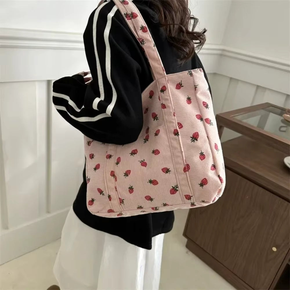 Person wearing a black hoodie with a pink tote bag featuring strawberry pattern.