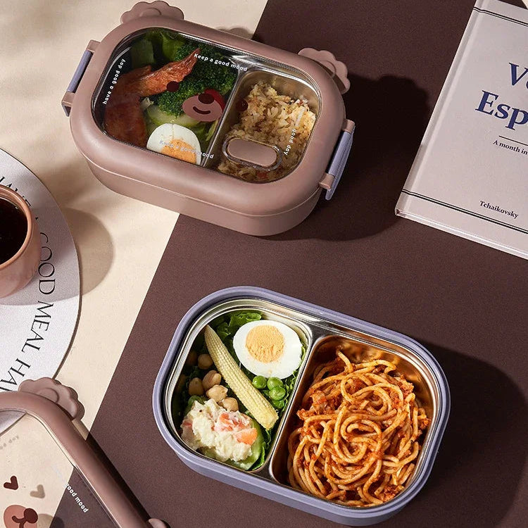 Two kawaii bento boxes with compartments of food on a brown surface with a book and fork.