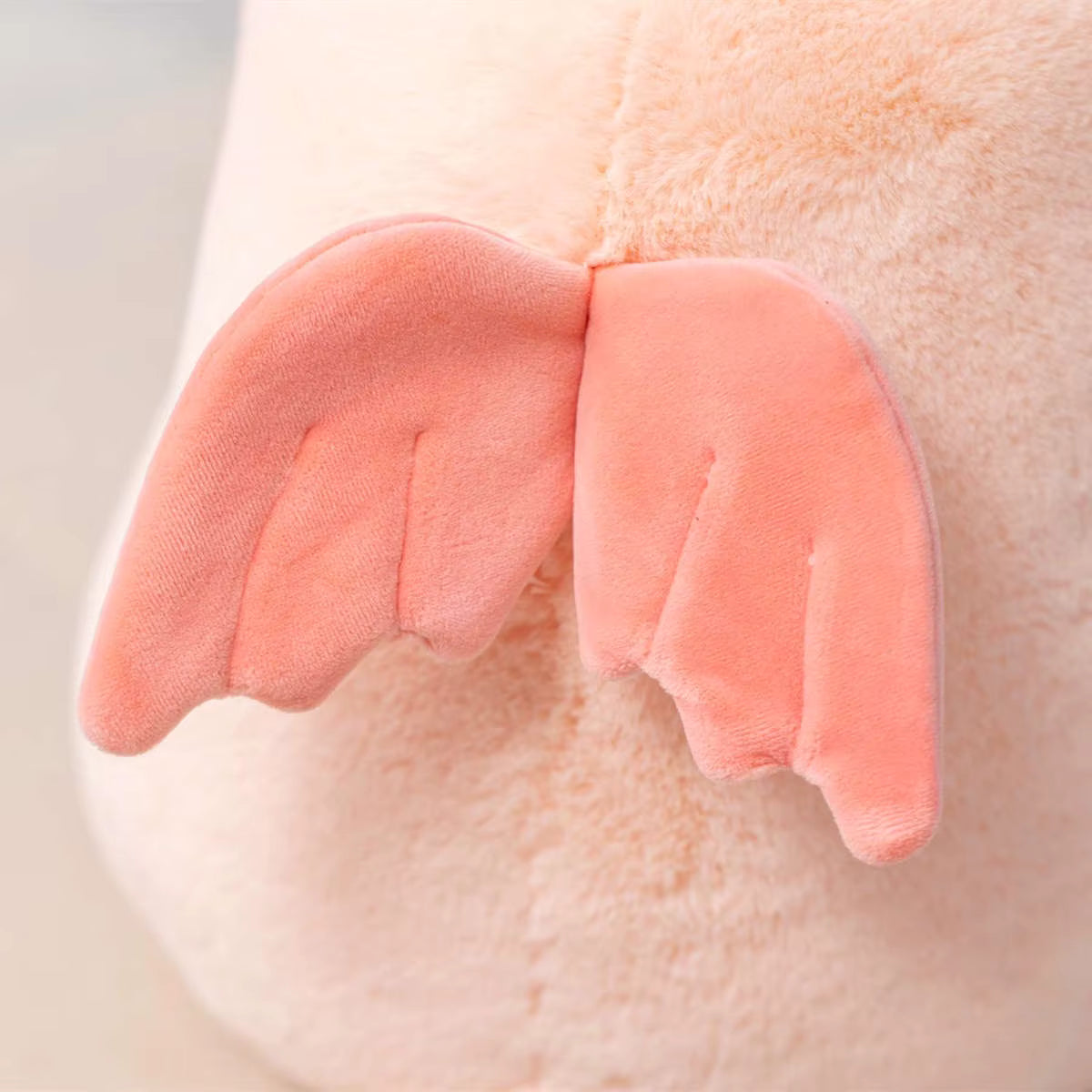 A close-up of a plush toy or soft stuffed animal with soft peach-pink wings attached to a pale blush-beige fuzzy body.