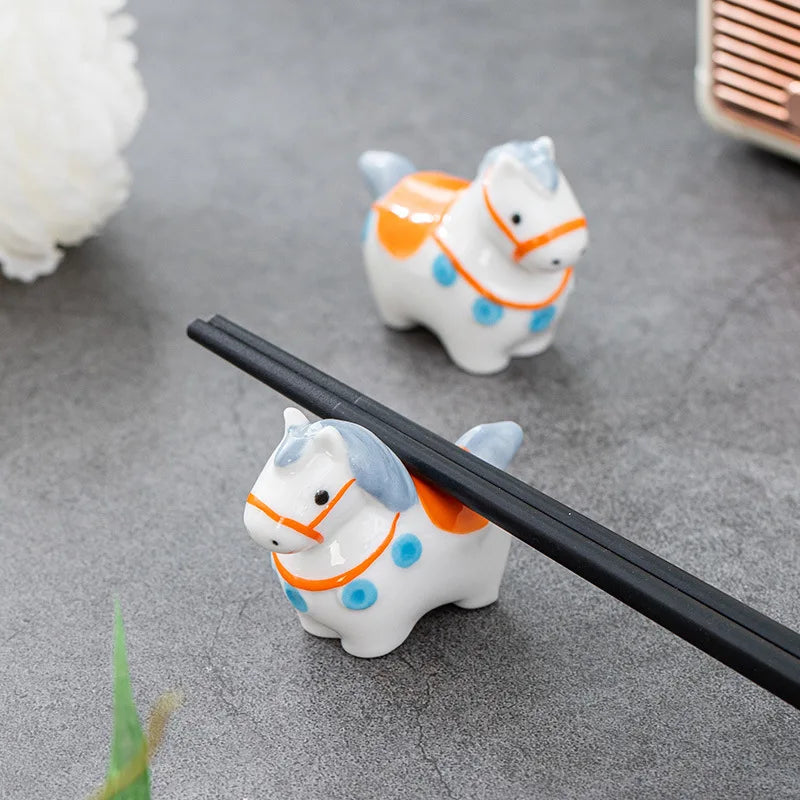 Two ceramic horse-shaped kawaii chopstick rests on a gray surface with a blurred background.