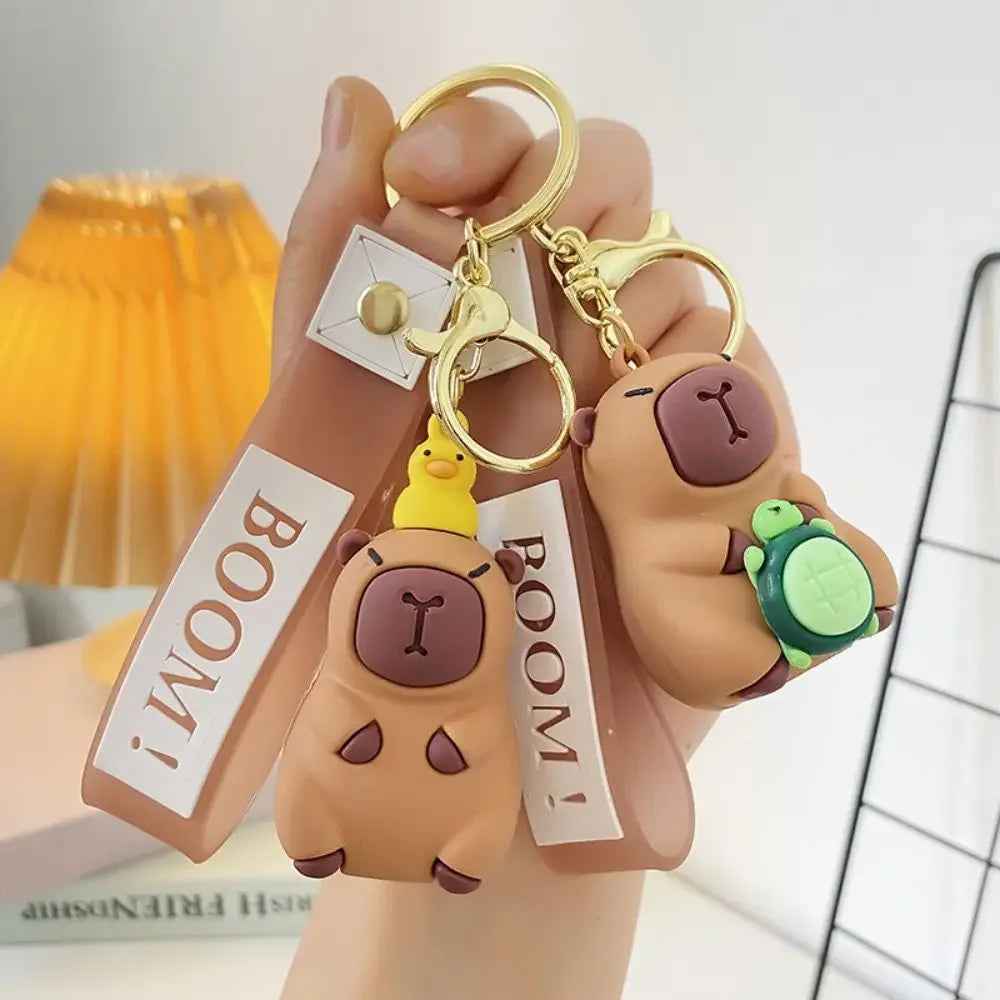 Keychain with kawaii bear design and 'BOOM!' text held by a hand against a blurred indoor background.