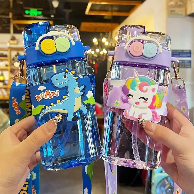 Two colorful kawaii water bottles with dinosaur and unicorn designs held by hands in a store setting.