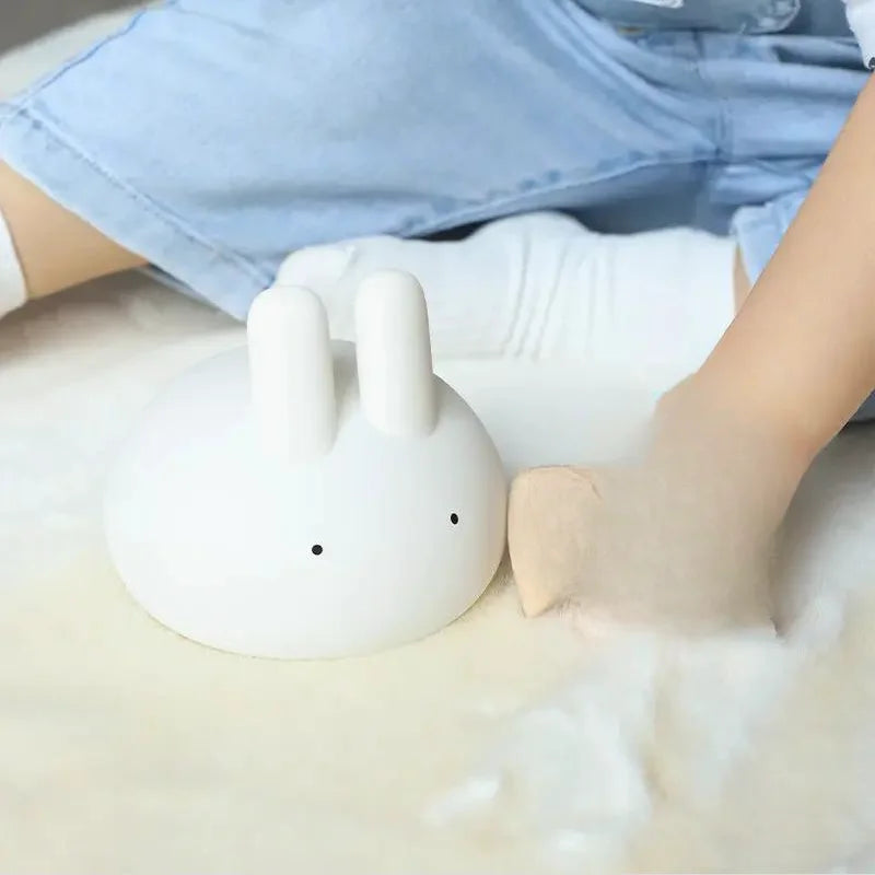 White rabbit-shaped kawaii night light on a white surface with a person wearing blue jeans in the background.