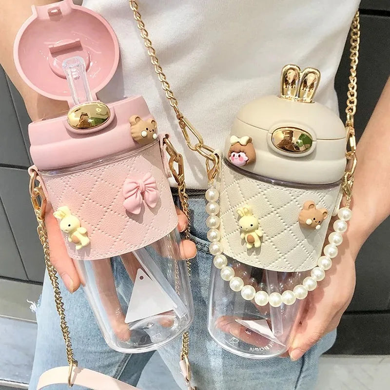 Two transparent kawaii water bottles with decorative tops held by a person, one pink and one beige with bear designs.