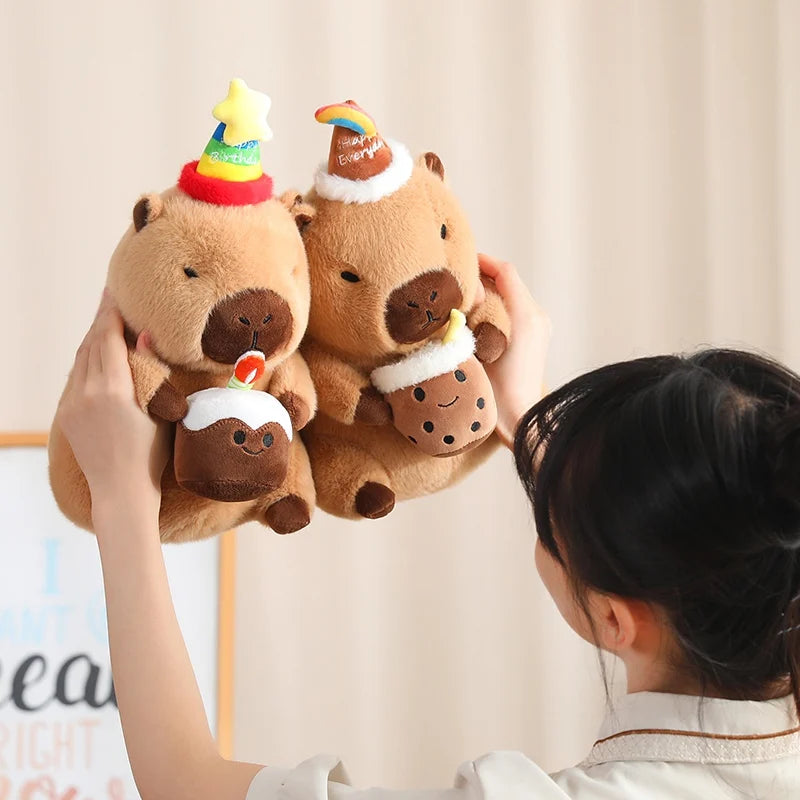 Person holding three small brown capybara plush toys with festive hats against a light background