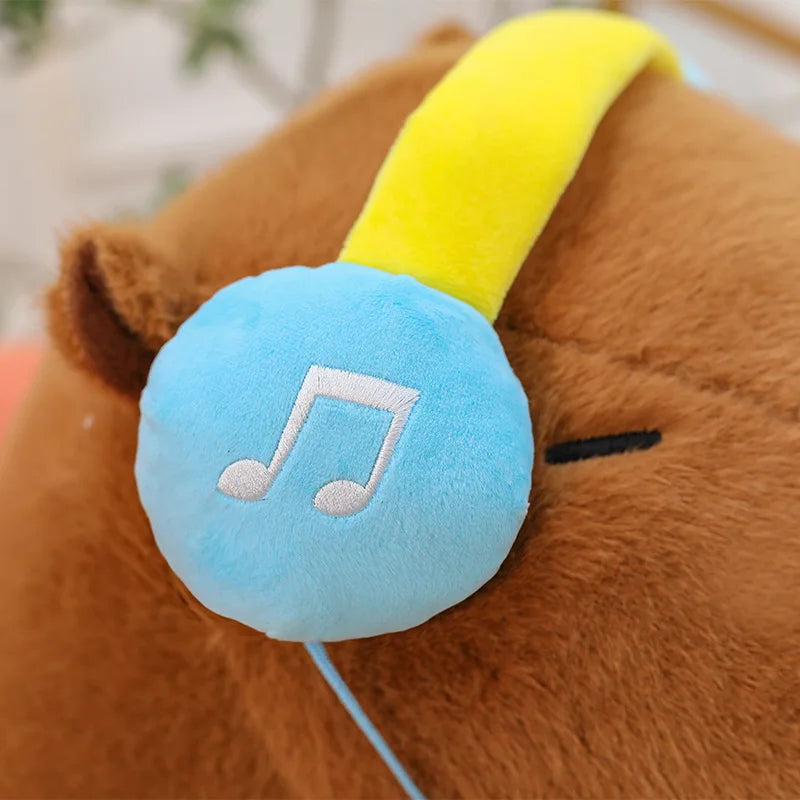 Capybara plush toy with yellow headband and blue earbud featuring a music note symbol.