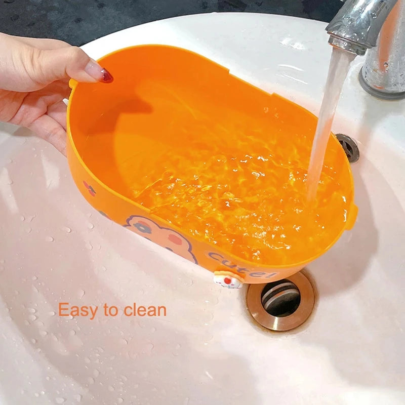 Orange silicone lid of a kawaii food container rinsed under running water in a sink with text 'Easy to clean'.