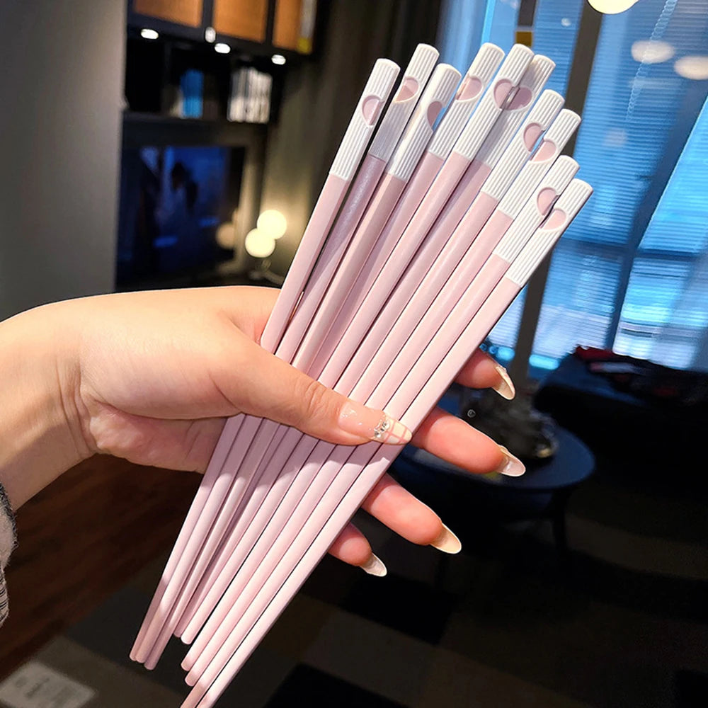 Hand holding a set of pink kawaii chopsticks with heart patterns in a blurred indoor setting