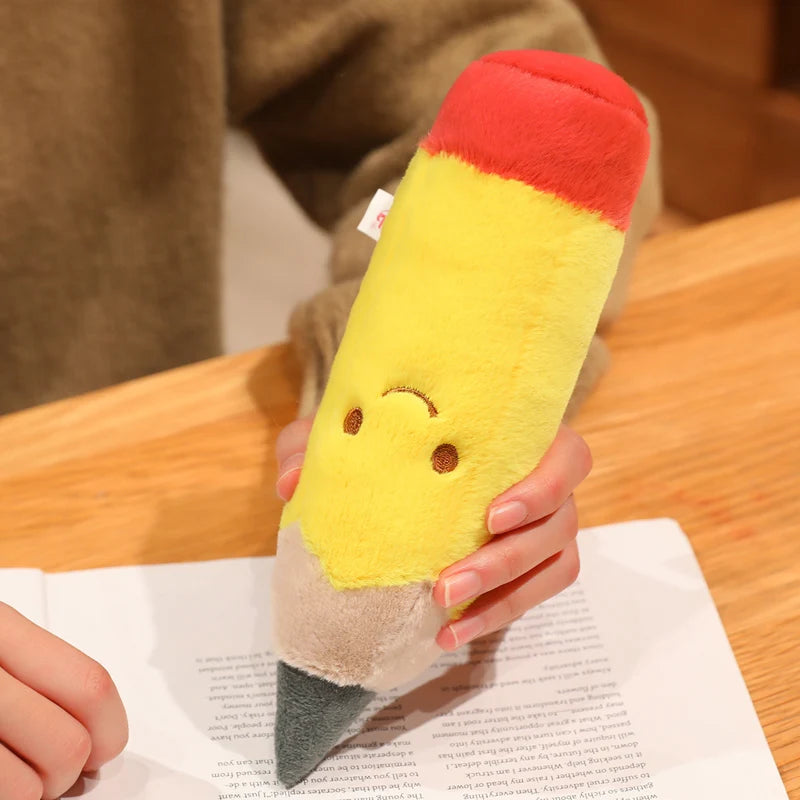Kawaii plush pencil-shaped toy with a smiley face held by a person on a wooden table.